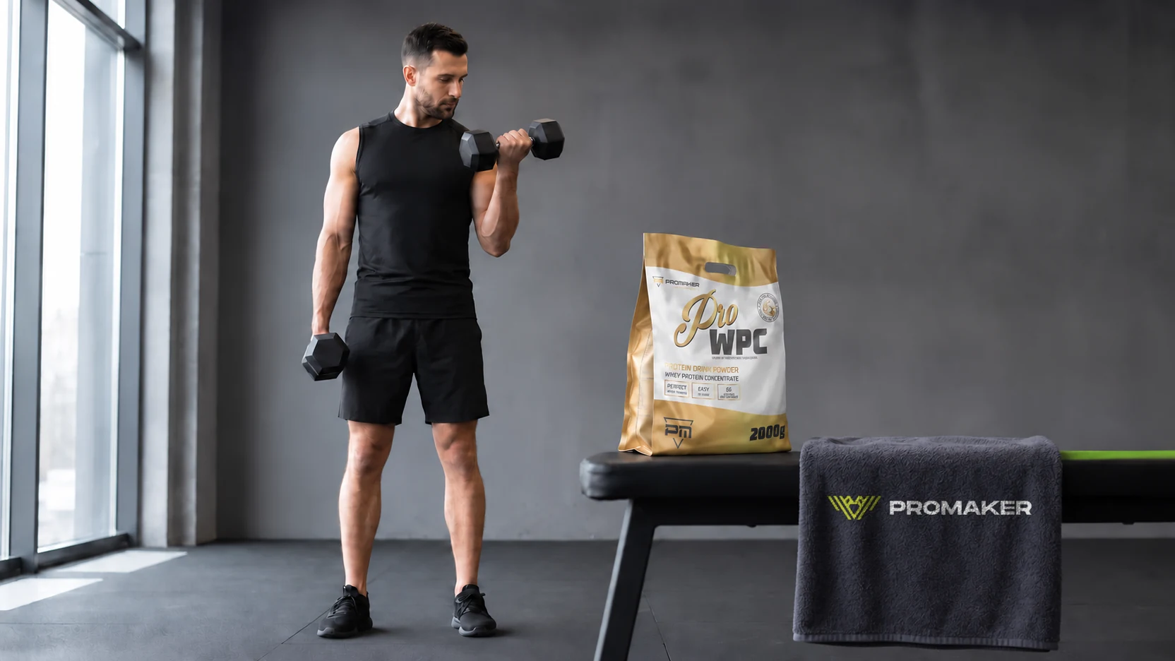 Ćwiczenia na biceps: mężczyzna robi uginanie ramion z hantlami, na ławce odżywka PROMAKER Pro WPC 2000 g
