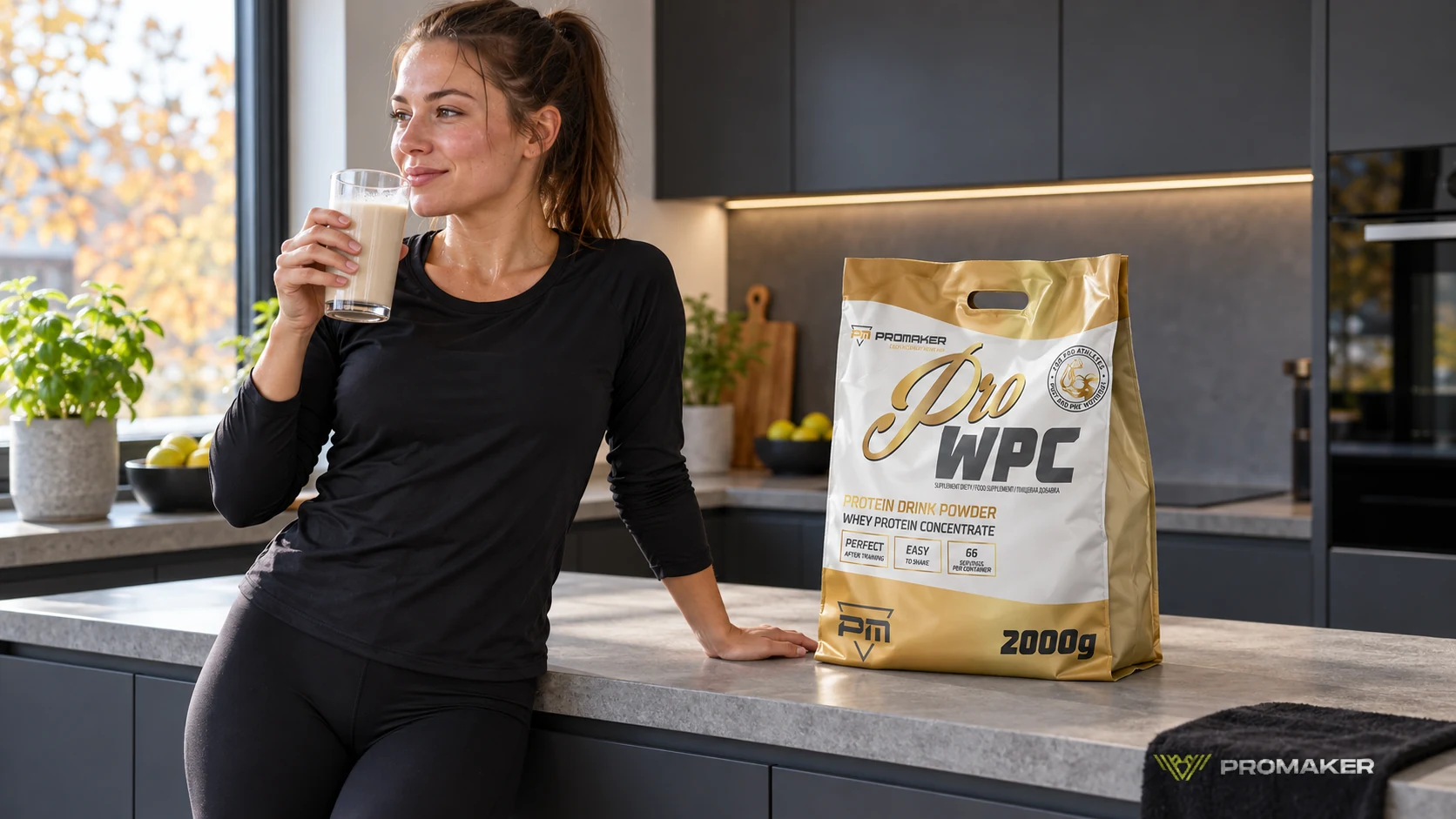 Biegaczka po pierwszym biegu pije shake w kuchni, obok odżywka Pro WPC PROMAKER i ręcznik z logo