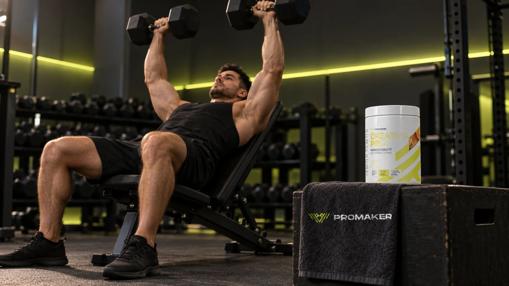Mężczyzna wyciska hantle na ławce skośnej na siłowni, obok kreatyna PROMAKER Creatine PRO+ i ręcznik z logo